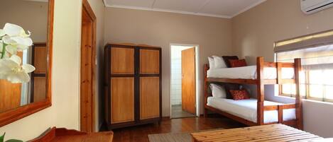 Una habitación con armario de madera, camas literas, un espejo y una ventana con persianas.