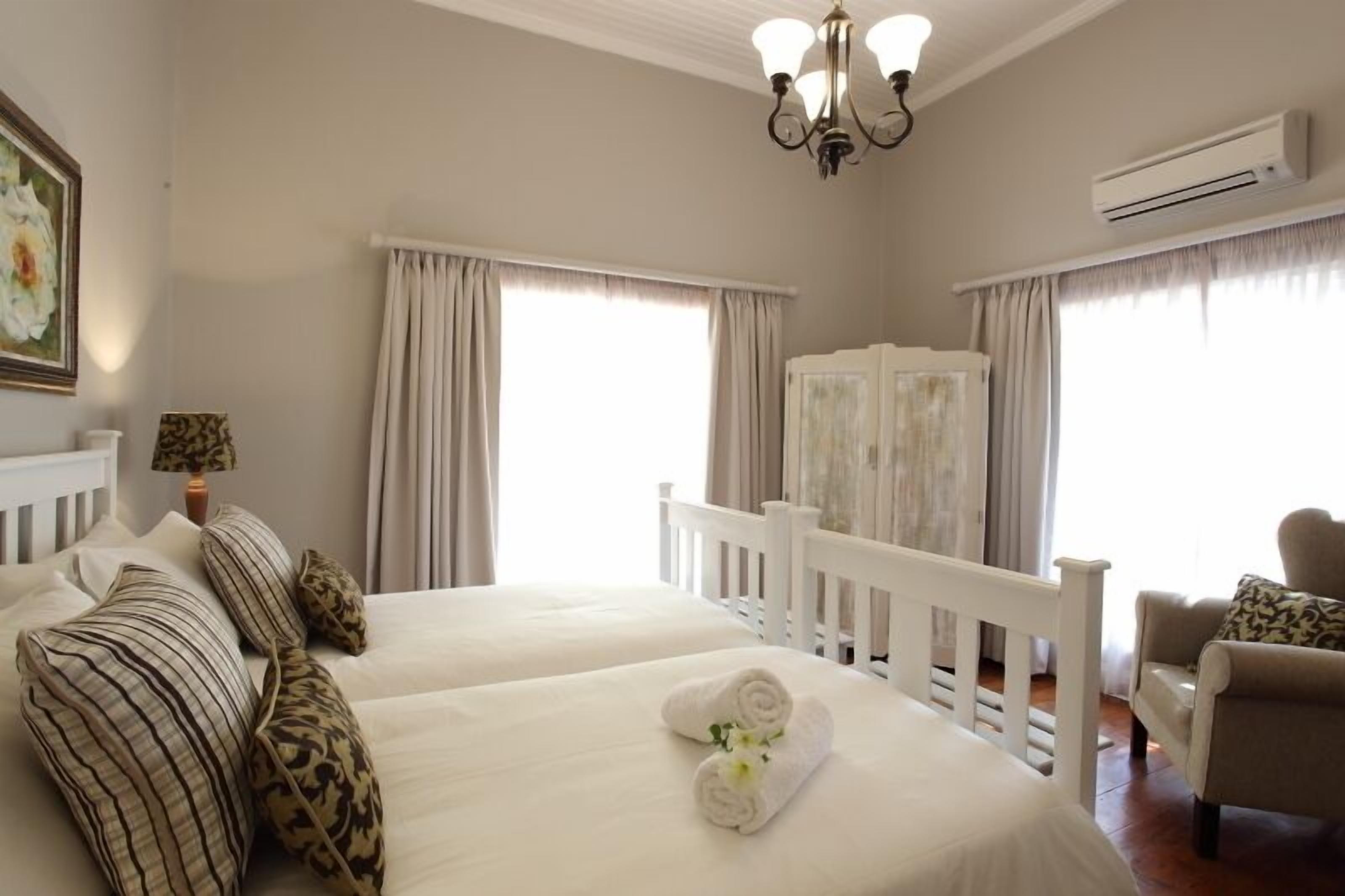 Habitación de hotel con dos camas, una silla blanca y un ventanal con cortinas.