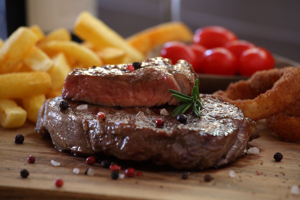 A steak with fries and cherry tomatoes on a wooden board.