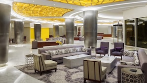 En rummelig lobby med moderne design, der inkluderer et stort opholdsområde med sofaer og lænestole, et receptionsskranke samt et iøjnefaldende loft med geometriske mønstre.