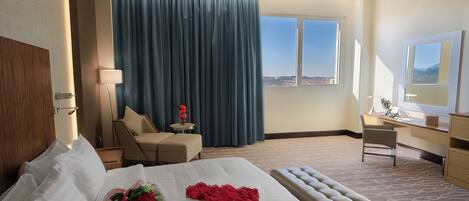 A hotel room with a large bed, a desk, a chair, a window with a view, and a curtain.