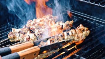 Grilled chicken skewers on a barbecue grill with visible flames and smoke.