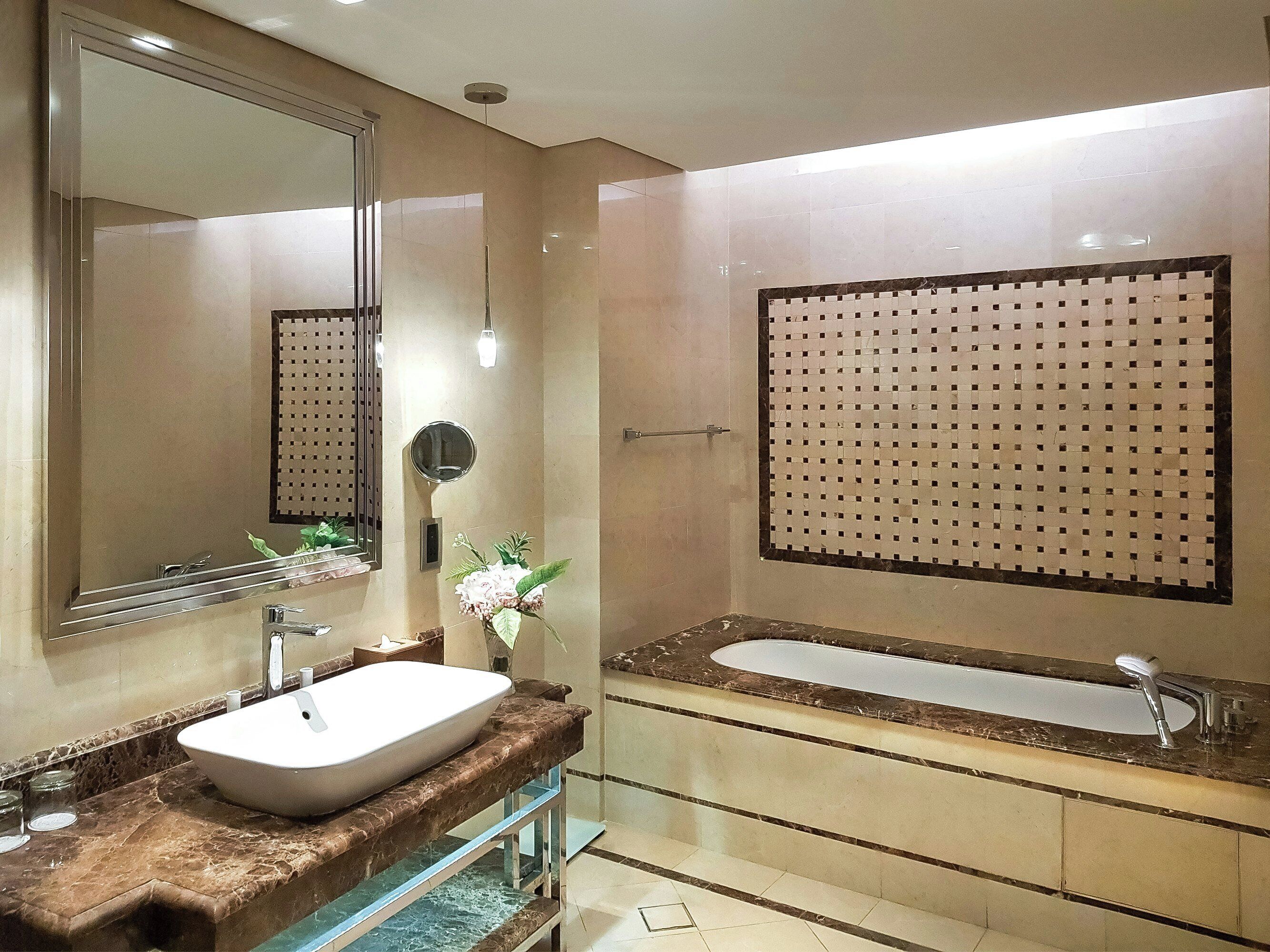 A modern bathroom with a large mirror, a white sink, a bathtub, and a decorative wall panel.