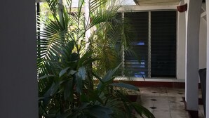 Un espacio al aire libre techado con suelo de baldosas, plantas en macetas y una ventana con persianas.