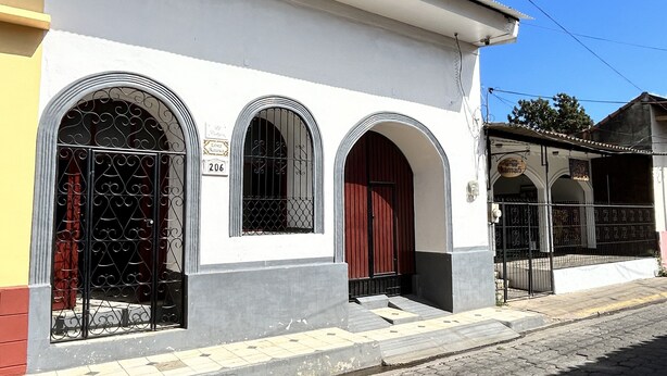 Un edificio con fachada blanca, tres ventanas de arco con rejas de metal, una puerta roja y un cartel que indica el número 206.