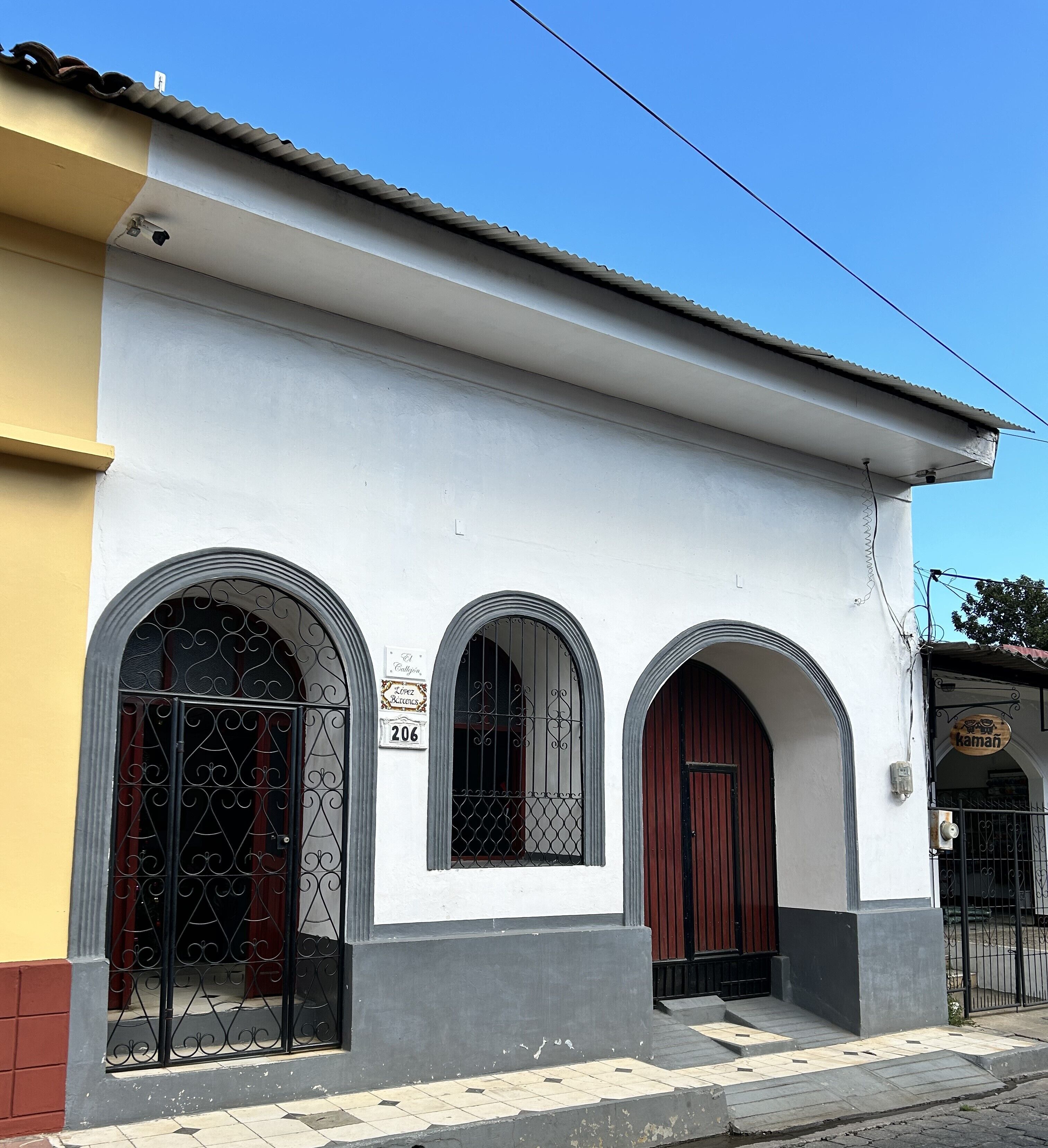 A building with three arched windows and a red door, a visible address sign, and a small entrance with steps.