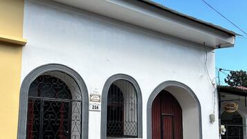 A building with three arched windows and a red door, a visible address sign, and a small entrance with steps.