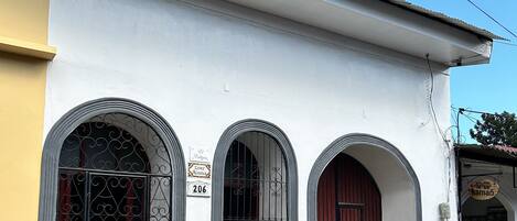 A building with three arched windows and a red door, a visible address sign, and a small entrance with steps.