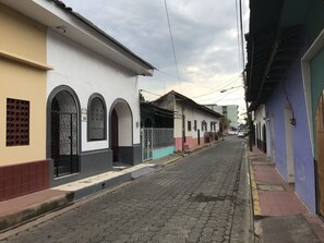 A narrow street lined with buildings featuring arched windows and doors, a paved road, and overhead power lines. - El Callejon Guest House (León)