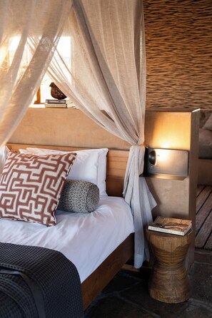 A bed with a canopy, a bedside lamp, and a wooden nightstand with a book.