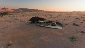 Un paysage désertique avec un seul bâtiment doté d’un toit de chaume, d’un espace extérieur aménagé pour s’asseoir et d’une tente.