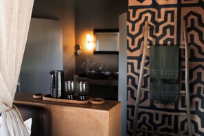 A room with a wooden side table holding a tray with two glasses and a pitcher. A patterned wall and a ladder leaning against it are visible.