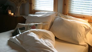 A bed with white linens and pillows, a vase with dried plants, and a candle on a wooden nightstand. - Skiff Point Guest House (Bainbridge Island)