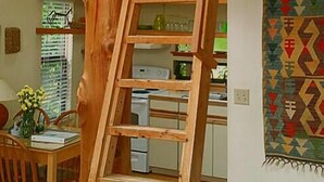 A wooden ladder against a wall in a room with a kitchen area visible in the background. - Skiff Point Guest House (Bainbridge Island)