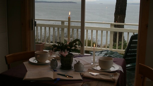 A balcony with a table set for tea, a candle, and a view of the sea. - Skiff Point Guest House (Bainbridge Island)
