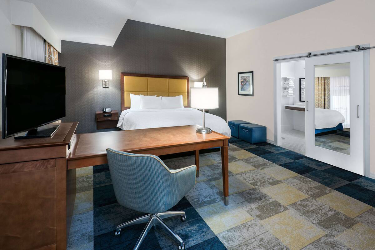 Une chambre d’hôtel équipée d’un lit, d’un bureau, d’une chaise, d’une télévision et d’un grand miroir.