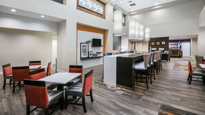 Un hall d’hôtel moderne avec un îlot central, des espaces de détente et une cuisine en arrière-plan.