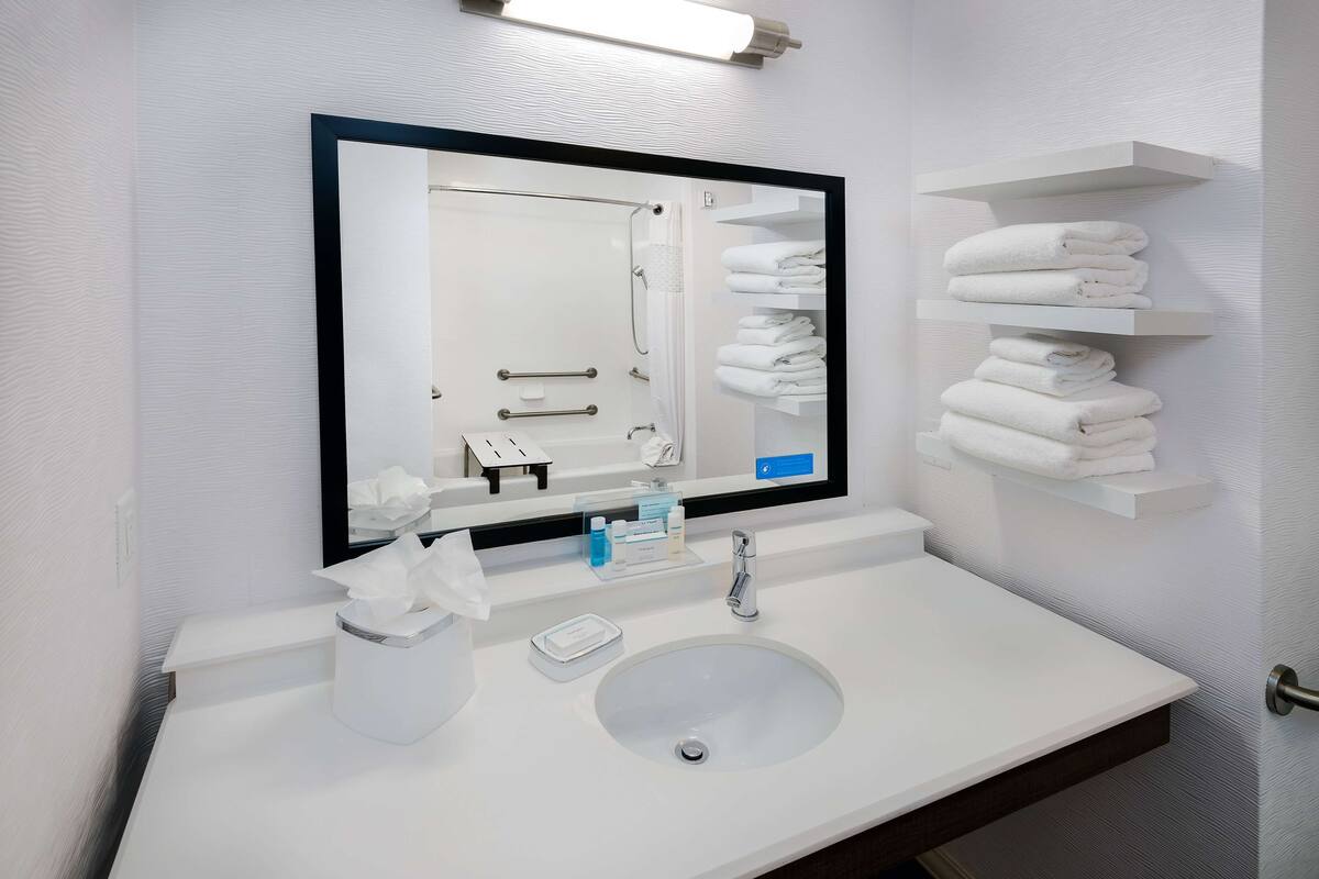 Une salle de bain moderne avec un grand miroir, un lavabo blanc et des porte-serviettes.