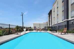 Piscina con sillas de descanso y una valla, rodeada de edificios.