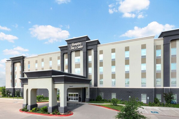 Un hotel Hampton Inn & Suites con una fachada moderna, un acceso cubierto y un estacionamiento.