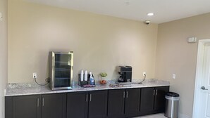 A kitchen with dark cabinets, a stainless steel refrigerator, a coffee maker, and a trash can. - Palace Inn 290 & Jones Rd (Houston)