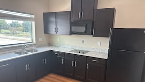 A kitchen with dark cabinets, a stainless steel sink, a microwave, and a refrigerator. - Palace Inn 290 & Jones Rd (Houston)