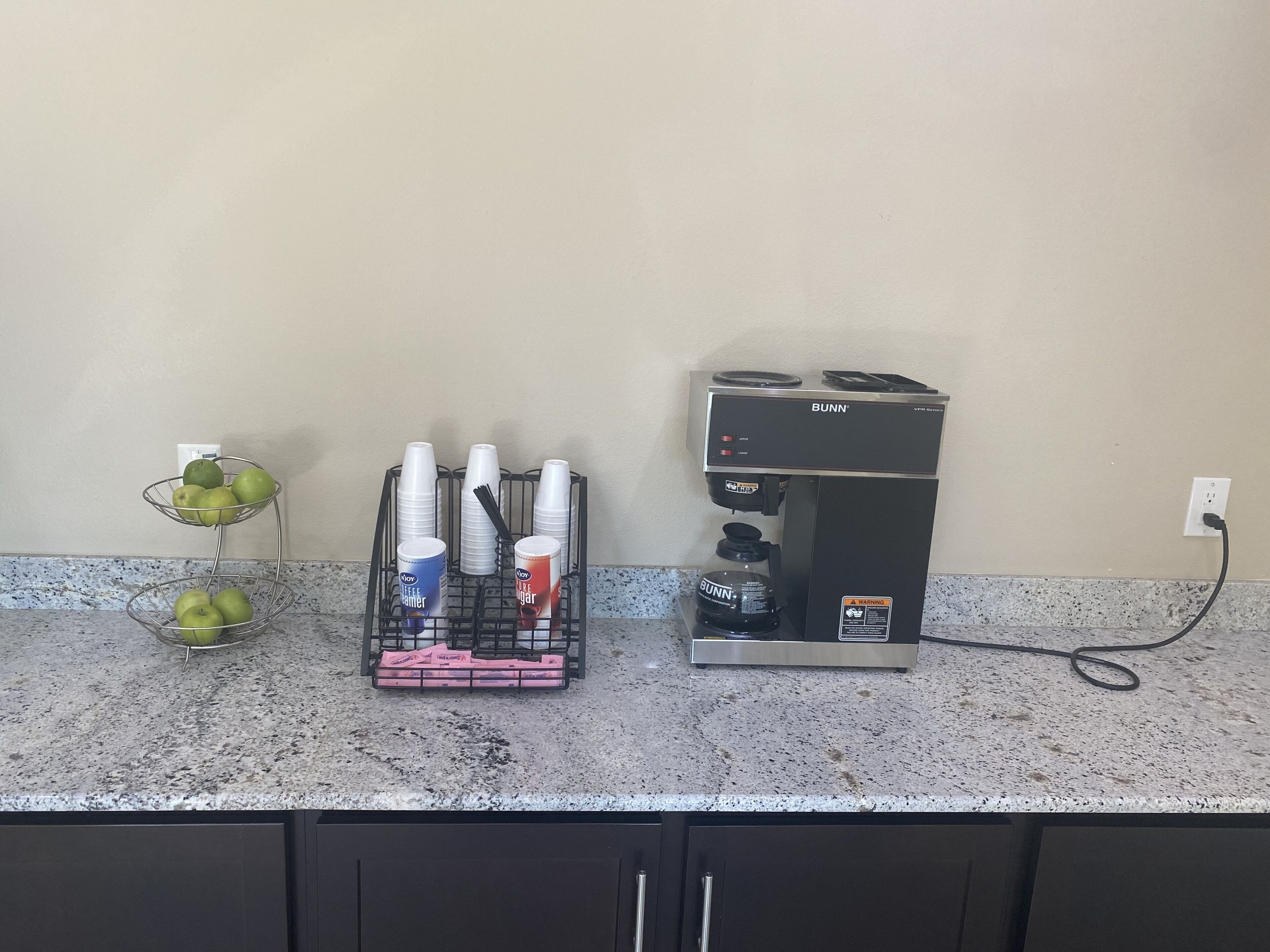 Uma bancada de cozinha com uma cafeteira, uma cesta de frutas e um porta-copos.