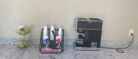 Uma bancada de cozinha com uma cafeteira, uma cesta de frutas e um porta-copos.