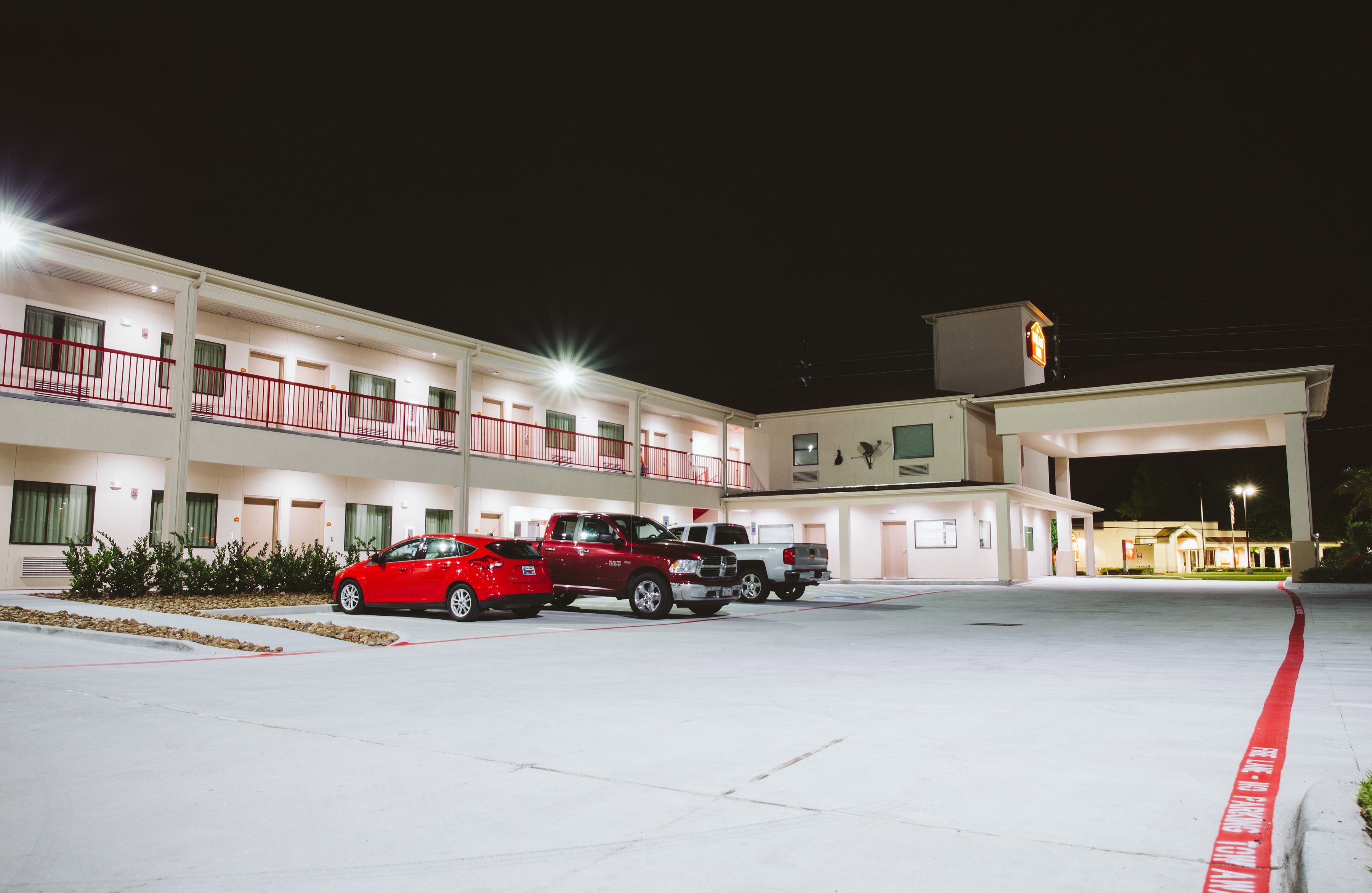 A motel with a parking lot, a red car, and a white truck parked in front.