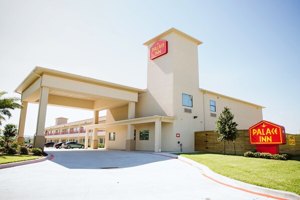 A hotel with a prominent sign, a covered parking area, and a well-maintained lawn.