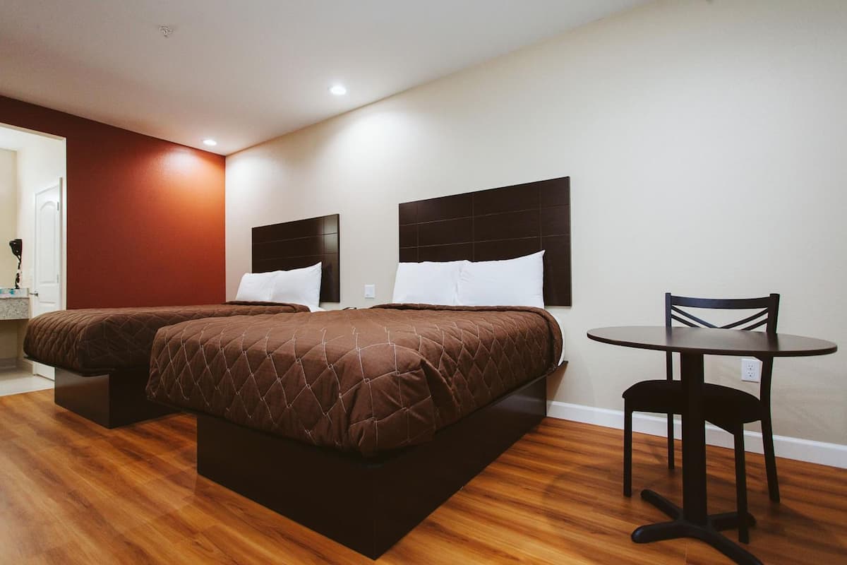 A hotel room with two beds, a small table, and a chair.