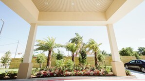A covered outdoor area with palm trees and a car parked nearby. - Palace Inn 290 & Jones Rd (Houston)