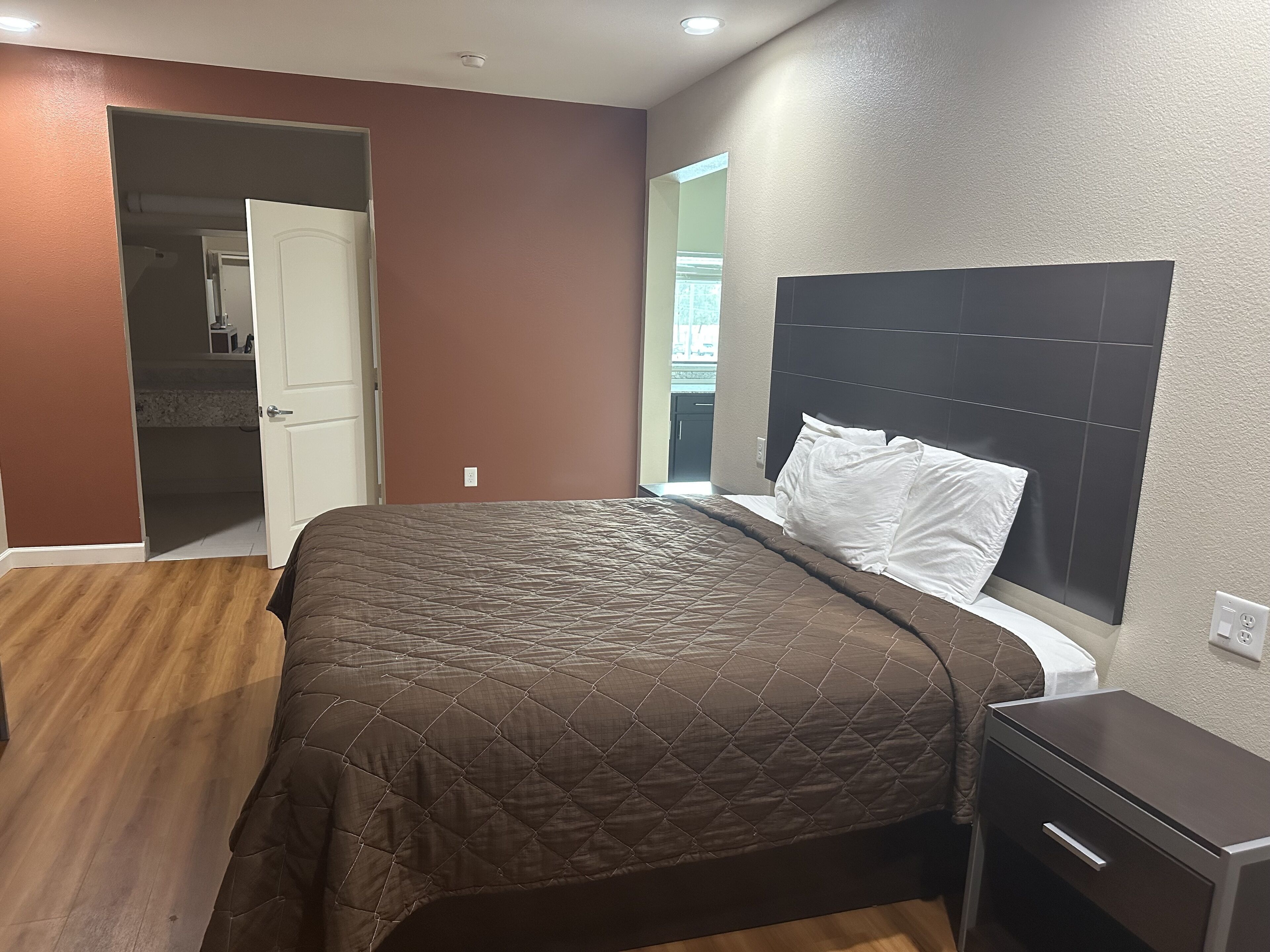 A bedroom with a bed, a nightstand, a wardrobe, and a bathroom visible through an open door.