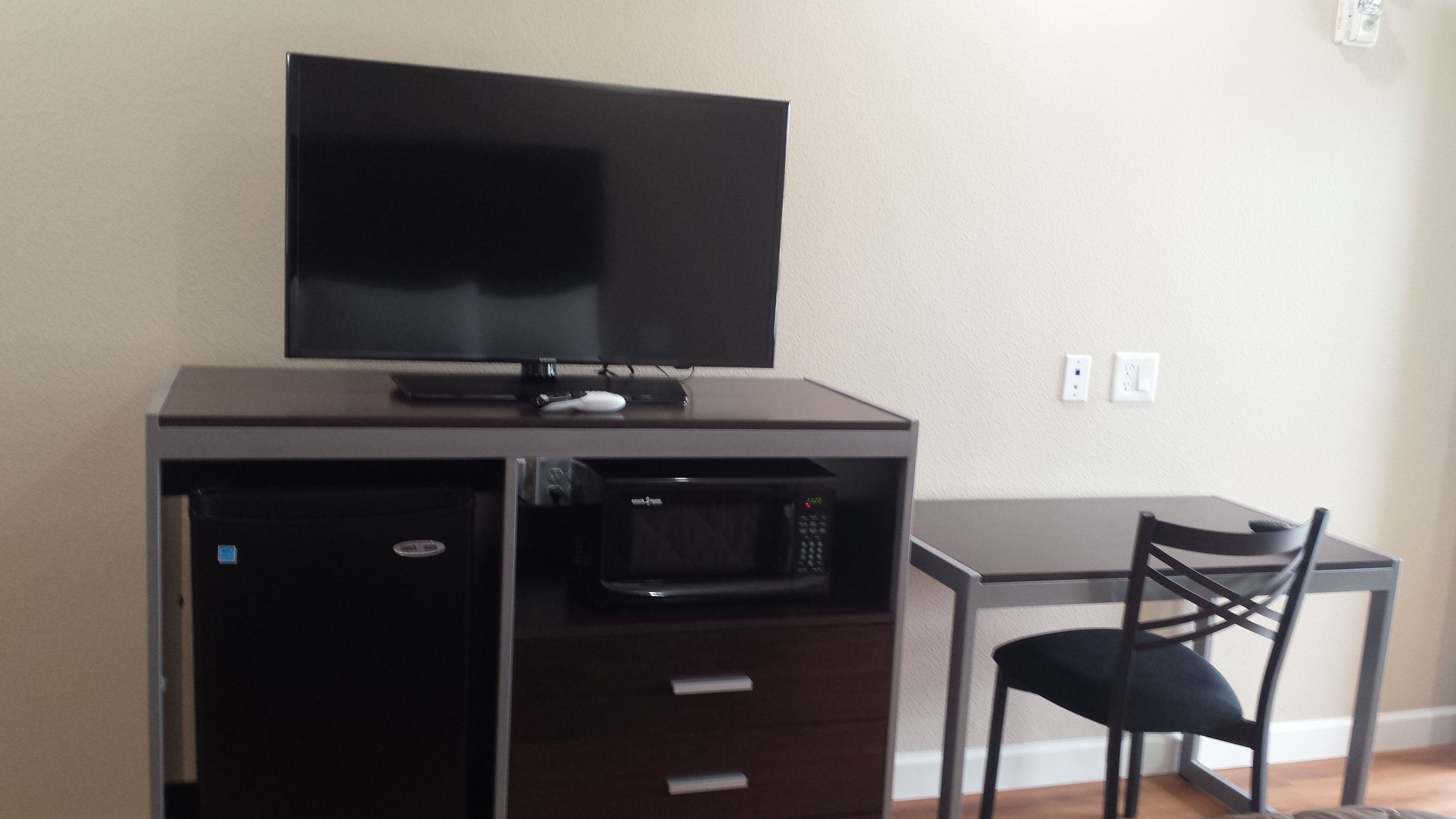 A compact kitchenette with a microwave, a small refrigerator, and a flat-screen TV on a wooden cabinet.