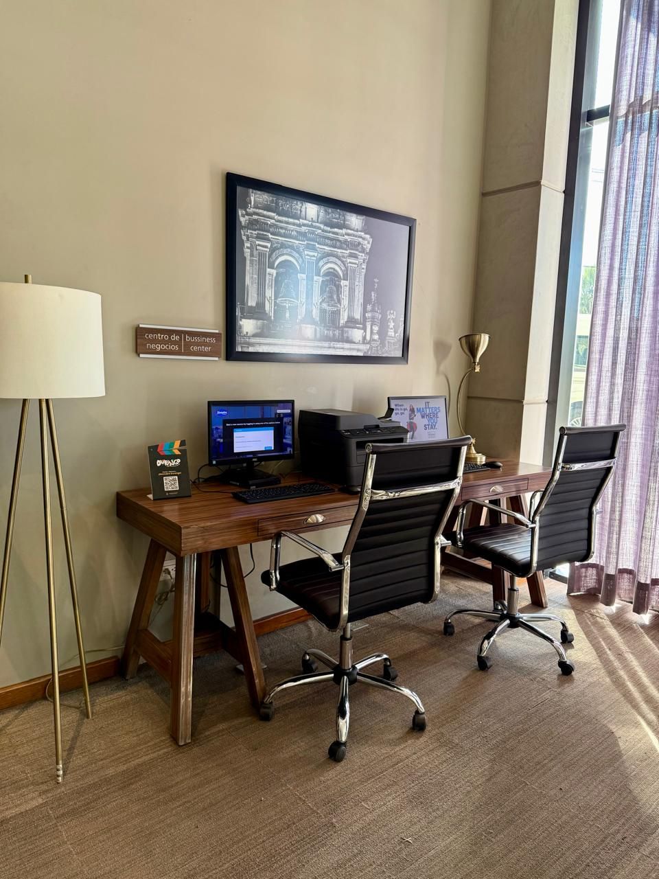 A business center with a desk, two chairs, a computer, a printer, and a framed picture on the wall.