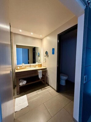 A modern bathroom with a large mirror, two sinks, a toilet, and a towel rack.
