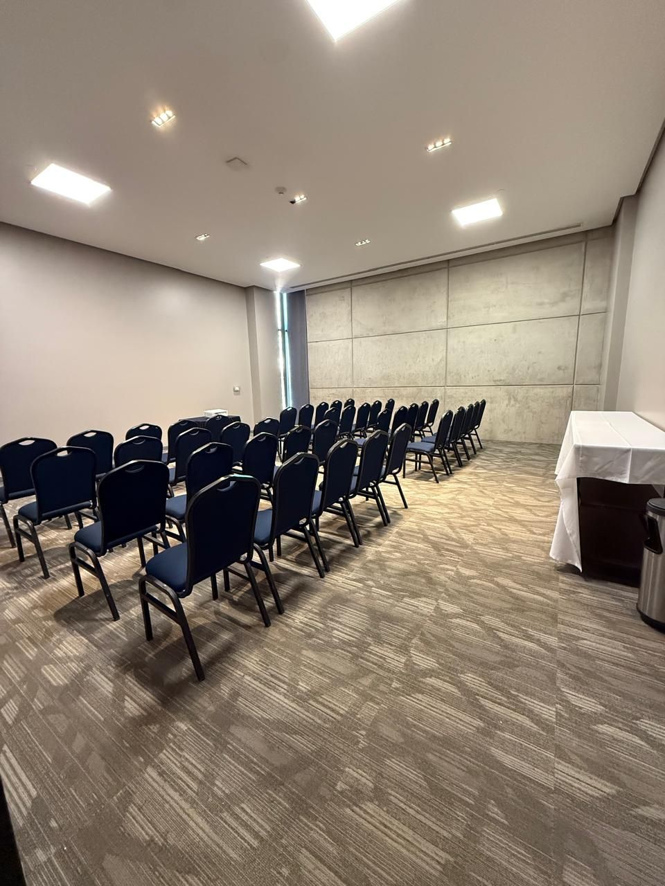A conference room with rows of chairs, a table, and a plain wall.