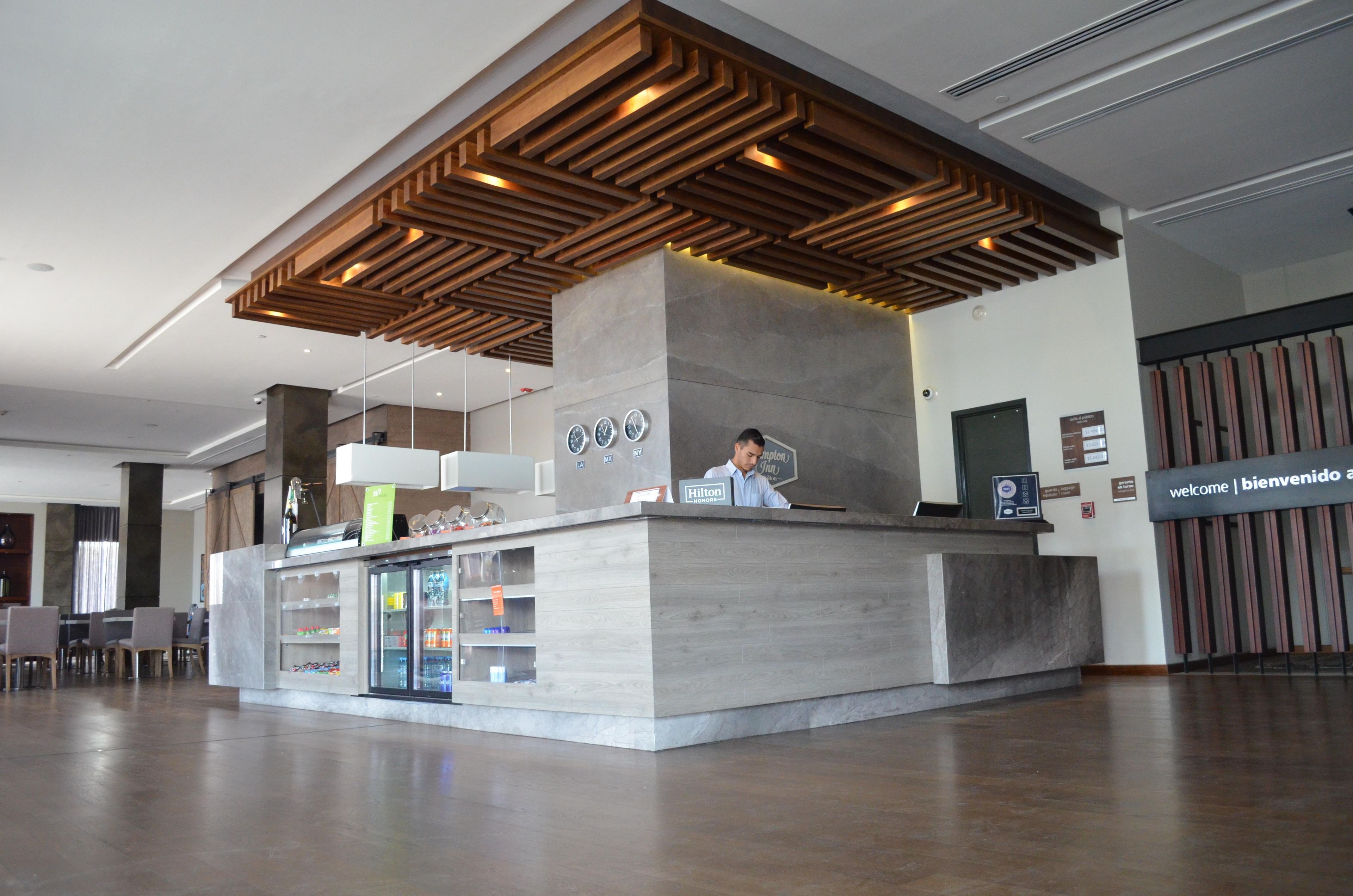 A modern reception desk with a wooden slatted ceiling, a glass display case with amenities, and a digital clock.