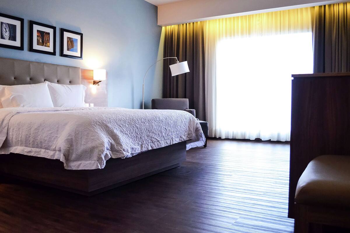A hotel room with a large bed, a nightstand, a desk, a chair, and a window with curtains.
