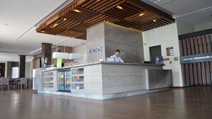Un moderno mostrador de recepción de hotel, con zona de estar con sillas y llamativo elemento decorativo de madera en el techo.