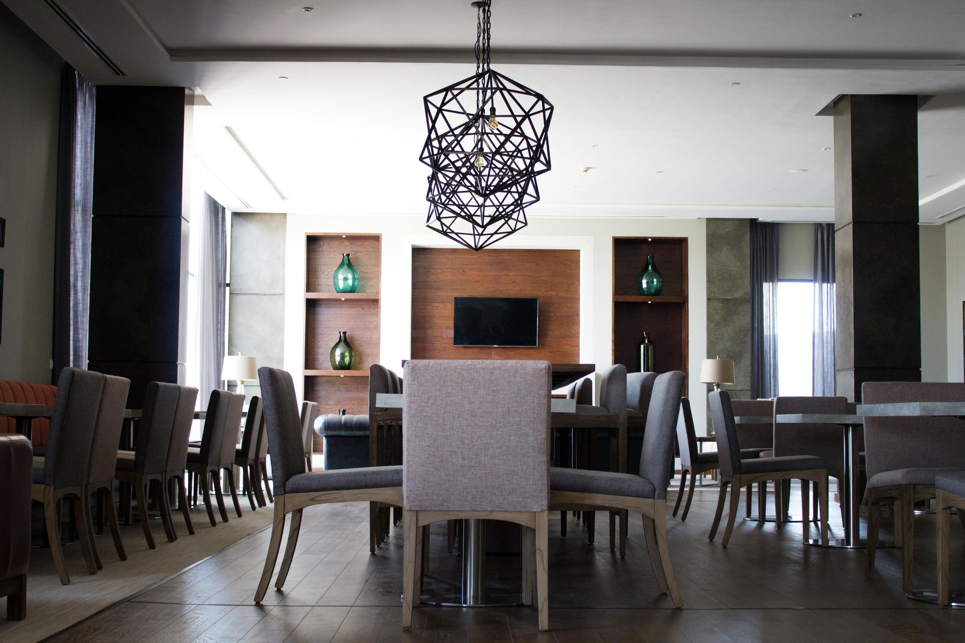 A modern interior with a dining area, chairs, a table, a TV mounted on a wooden wall, and a geometric light fixture.
