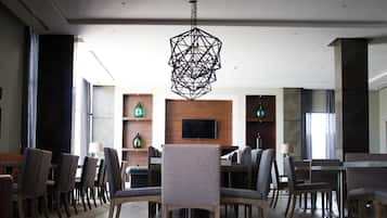 A modern interior with a dining area, chairs, a table, a TV mounted on a wooden wall, and a geometric light fixture.
