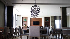 Un comedor moderno con una lámpara colgante de diseño geométrico, sillas de madera y un televisor de pantalla plana en la pared.