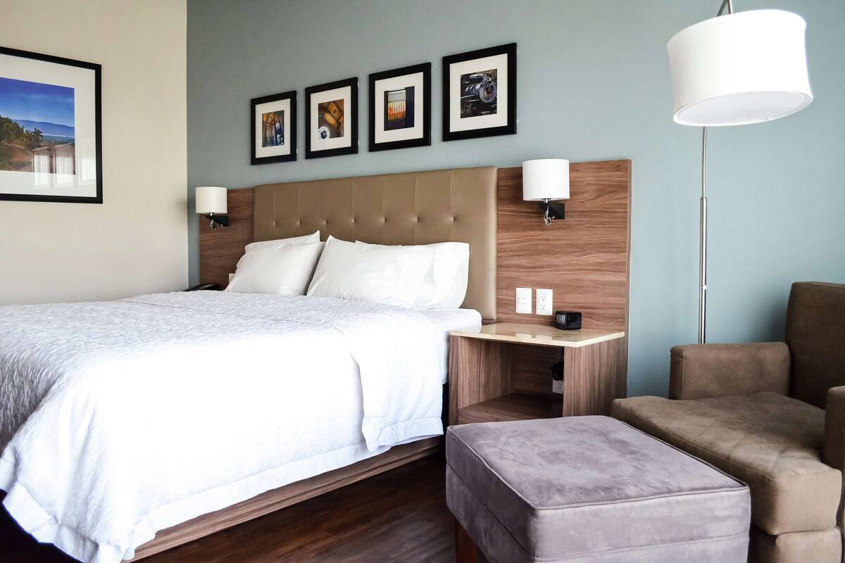 A hotel room with a large bed, two bedside tables, a nightstand, a floor lamp, and a seating area.