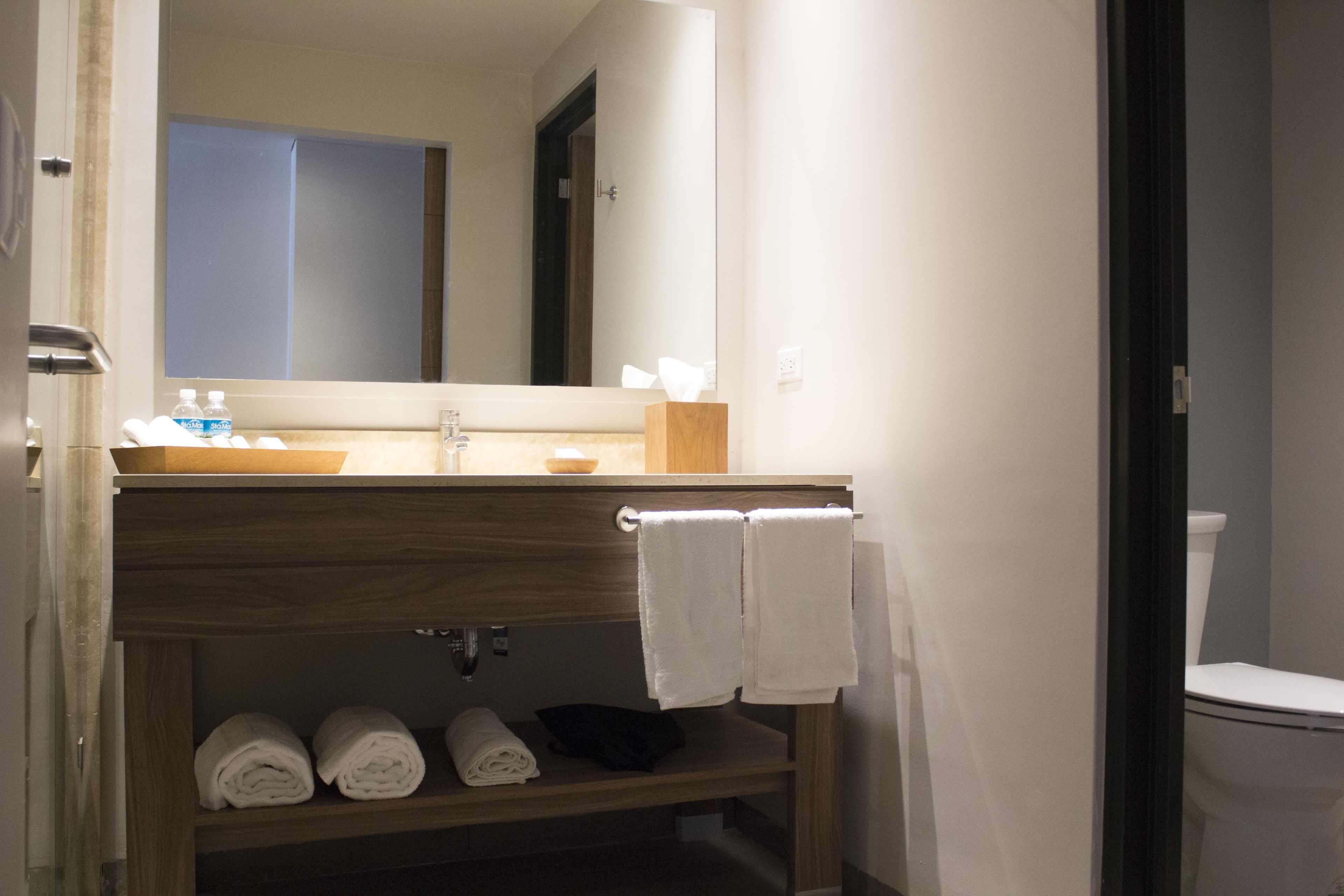 Un baño con tocador de madera, espejo, lavamanos y inodoro. Hay toallas y artículos de aseo en el tocador.