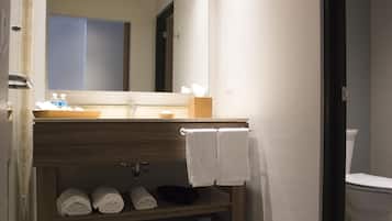 Un baño con tocador de madera, espejo, lavamanos y inodoro. Hay toallas y artículos de aseo en el tocador.