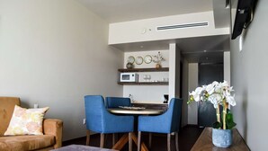 A modern living room with a sofa, a coffee table, and a dining area with blue chairs and a small table.