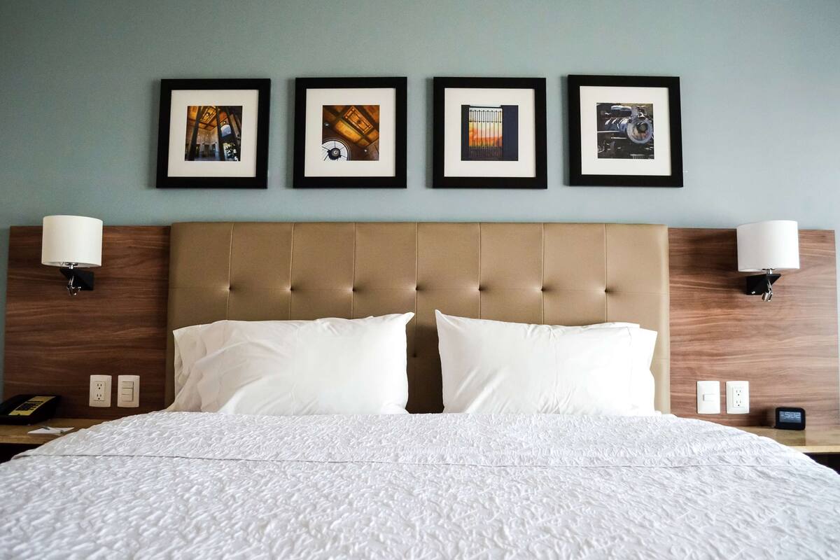 A hotel room with a large bed, two wall-mounted lamps, and four framed pictures on the wall.