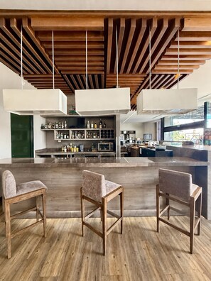 A modern bar area with wooden ceiling beams, hanging pendant lights, and a bar counter with a wine rack. There are three upholstered bar stools. - Hampton Inn by Hilton Durango (Durango)