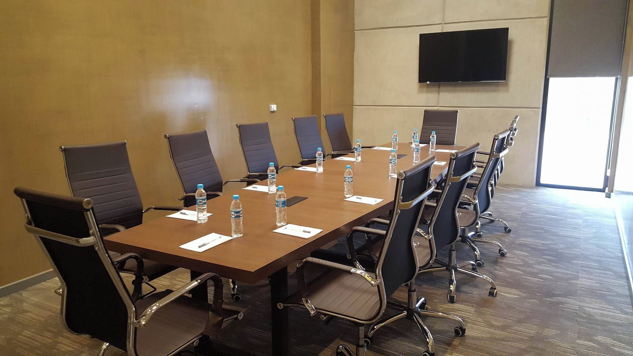 A conference room with a long table, chairs, water bottles, name cards, and a TV on the wall.